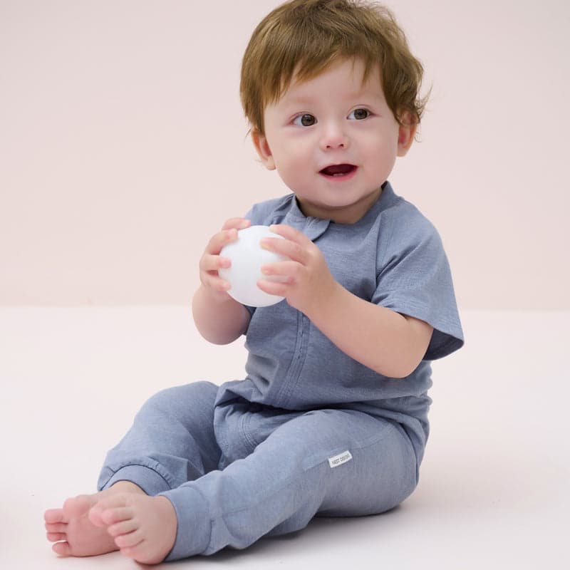 Nest Designs Bamboo Jersey Short Sleeve Slant Opening Romper Troposphere blue, baby sits and holds a white ball.