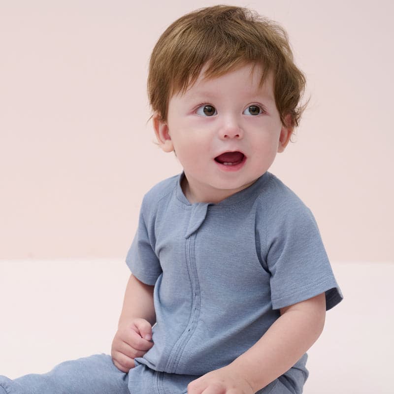 Nest Designs Bamboo Jersey Short Sleeve Slant Opening Romper Troposphere blue; baby sits up, showcasing the front slant zip.