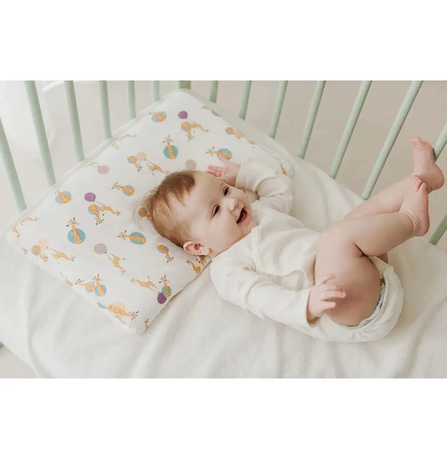 Nest Designs bamboo jersey toddler pillow and pillowcase with giraffe shapes, pictured in a crib with a smiling baby.