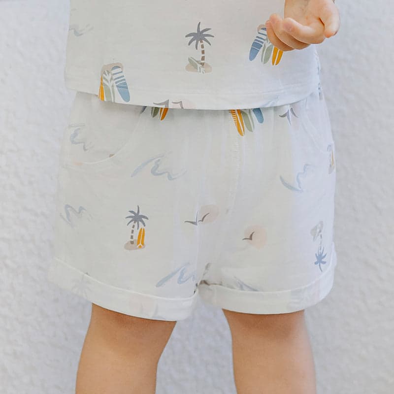 Nest Designs Bamboo Jersey Two-Piece Short Sleeve PJ Set Pastel Waves; toddler stands in white pajamas with pastel wave prints.