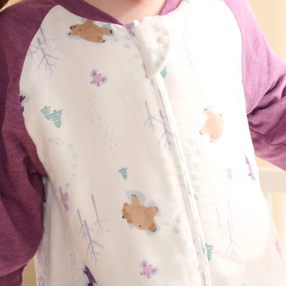 Nest Designs Bamboo Long Sleeve Footed Sleep Bag 1.0 Tog Snow Angels worn by a child in purple sleeves; cream with bear prints.