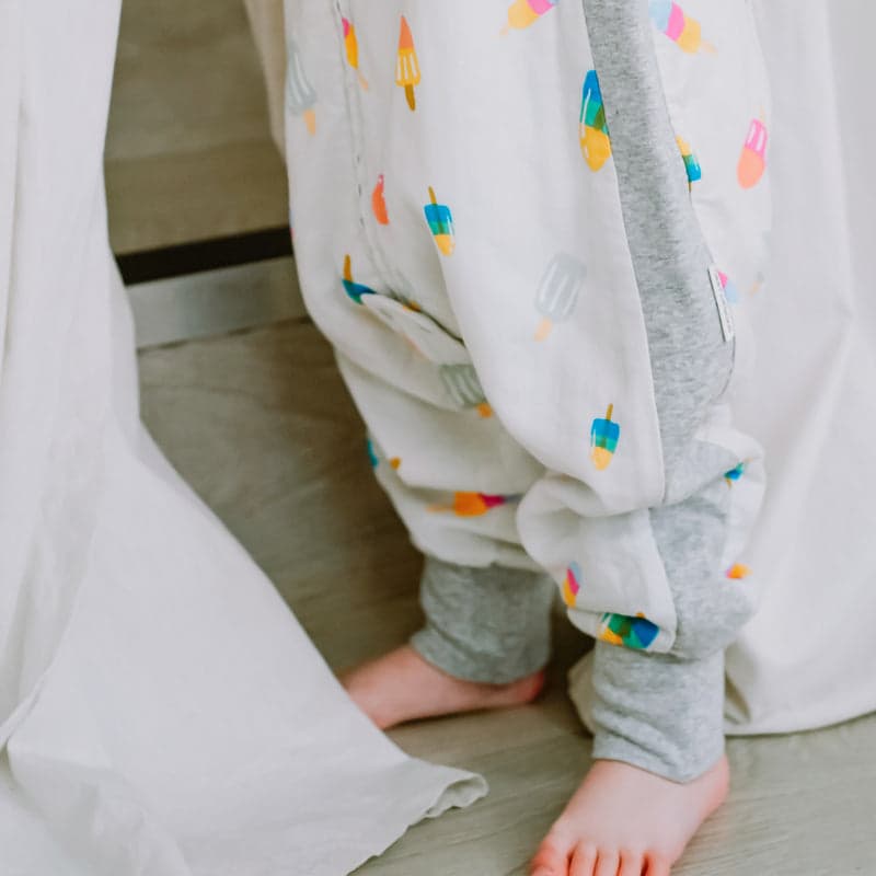 Nest Designs Bamboo Long Sleeve Footed Sleep Bag 1.0 Tog Summer Pops, white with colorful popsicle print and grey cuffs, toddler standing.