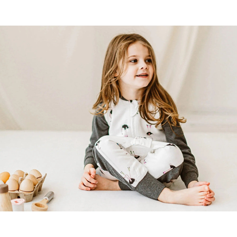 Nest Designs Bamboo Long Sleeve Footed Sleep Bag 1.0 Tog in white with pastel prints, worn by a toddler seated.