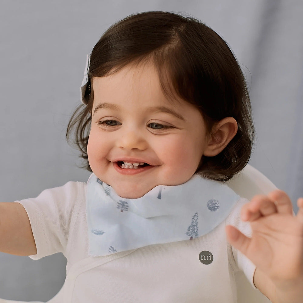 Nest Designs Bamboo Muslin Baby Bandana Bib Snowy Snuggles worn by a smiling toddler girl.