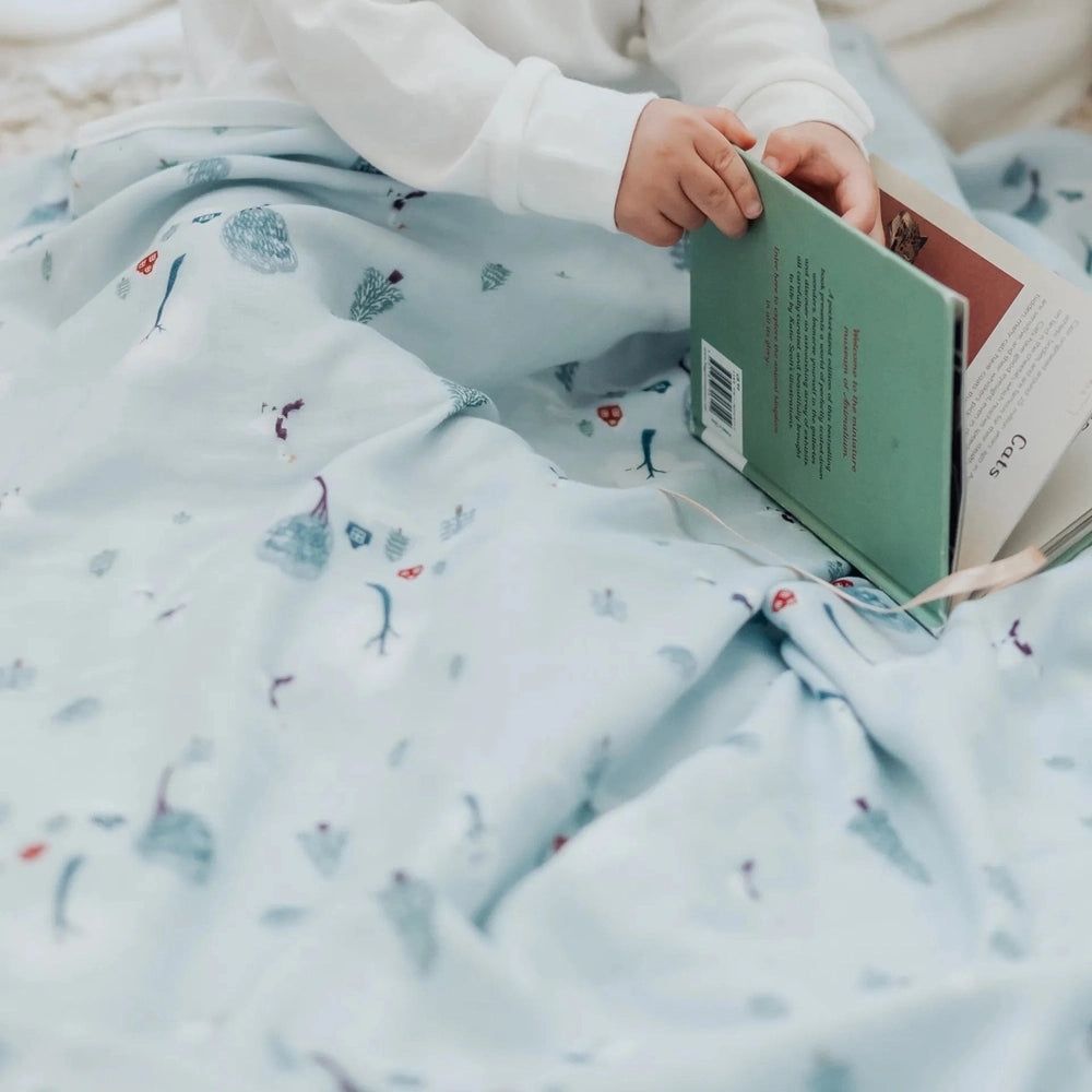 Nest Designs Bamboo Muslin Small Nesting Blanket, pale blue, baby wrapped and holding a book