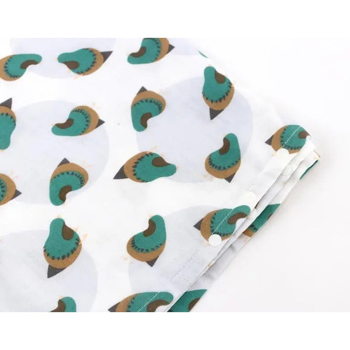 Nest Designs Bamboo Nursing Cover in white fabric with teal-brown circular pattern, showing metal snaps along edge.