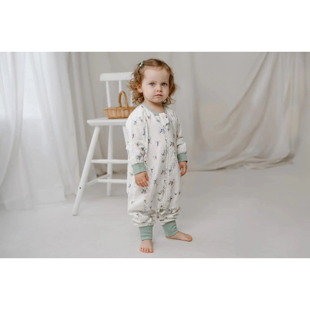 Nest Designs Bamboo Pima Long Sleeve Footed Sleep Bag 0.6 Tog Fairy Tale; toddler stands barefoot in white print sleep bag with mint cuffs.