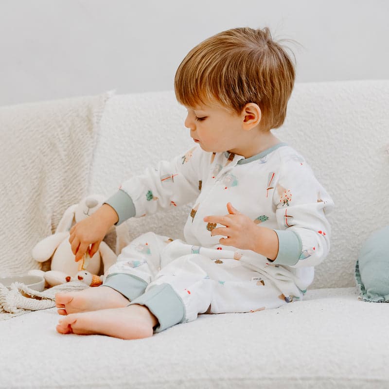 Nest Designs Bamboo Pima Long Sleeve Footed Sleep Bag Ice Cream Summer; toddler sits on couch in 0.6 TOG cozy footed sleepwear.