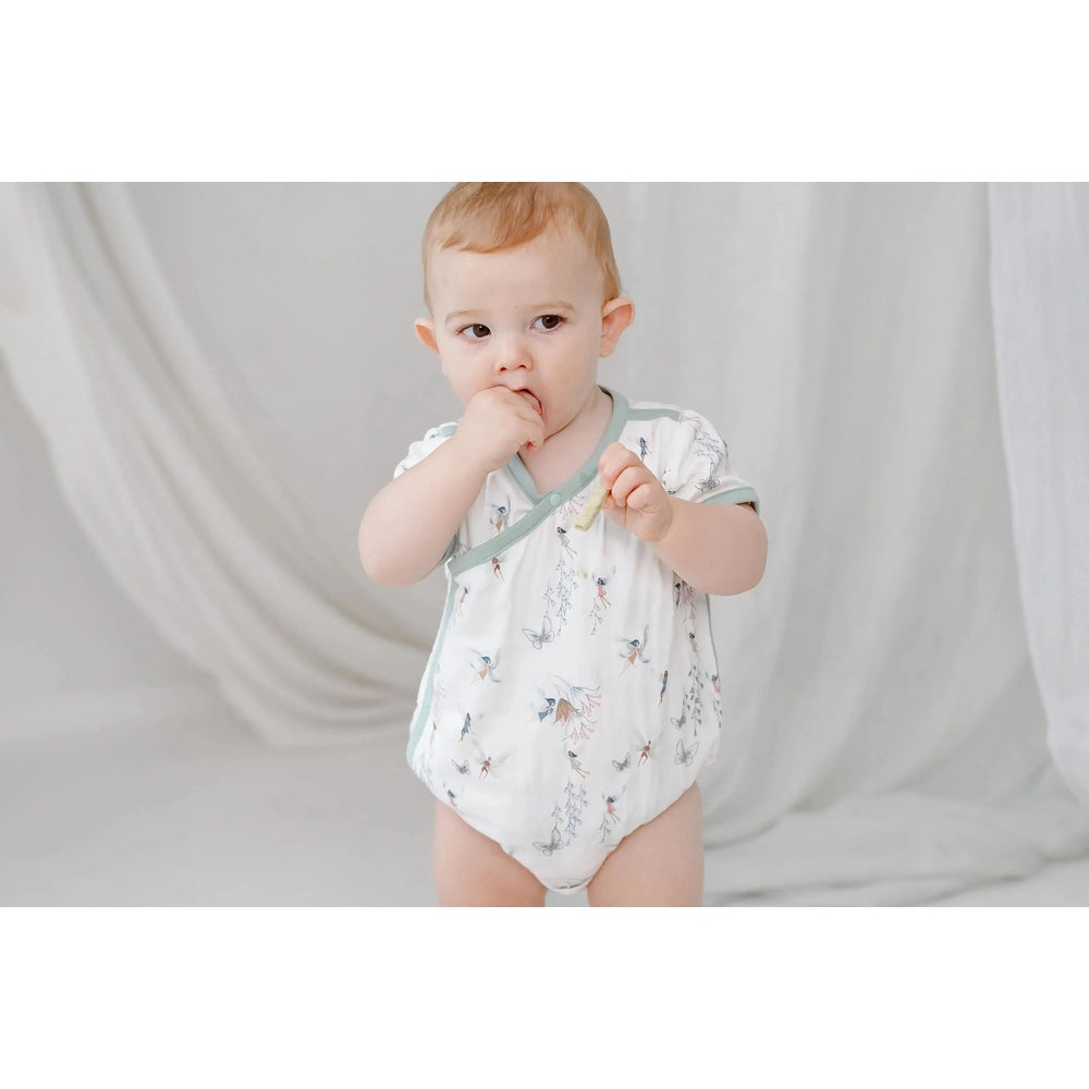 Nest Designs Bamboo Short Sleeve Kimono Onesie Fairy Tale, white with pastel butterfly print; baby stands, hand to mouth.