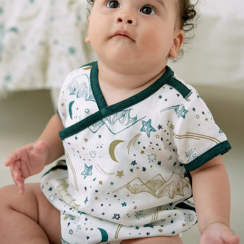 Nest Designs Bamboo Short Sleeve Kimono Onesie Stars White; baby sits up in white outfit with green trim and starry print