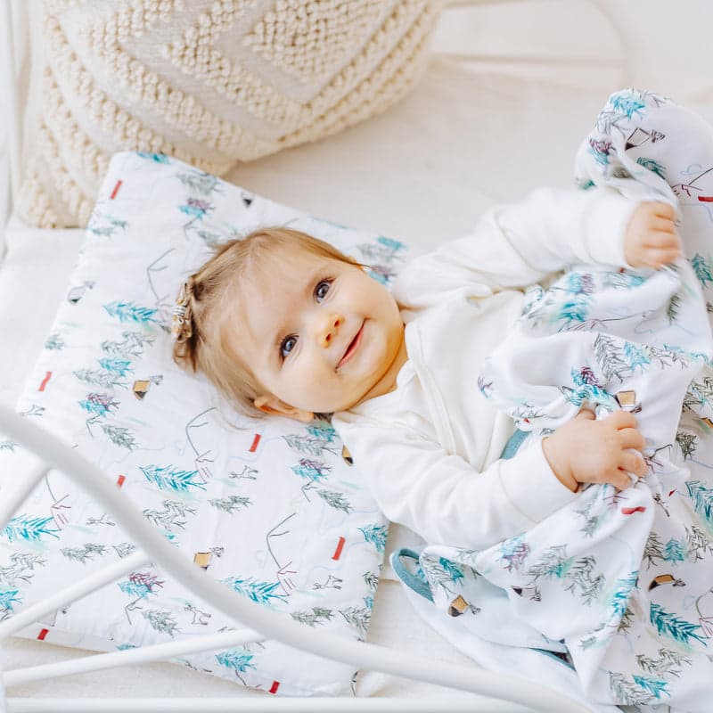 Nest Designs Bamboo Silk Toddler Pillow and Pillowcase Happy Trails; toddler rests smiling on the teal-print pillow and blanket.