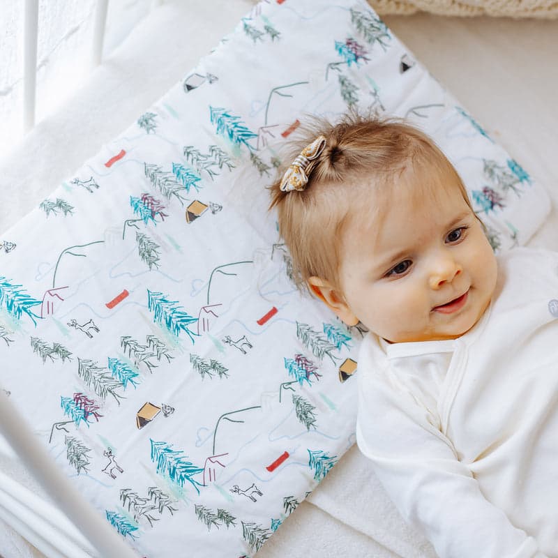 Nest Designs Bamboo Silk Toddler Pillow and Pillowcase Happy Trails; white fabric with teal trees, baby resting on it