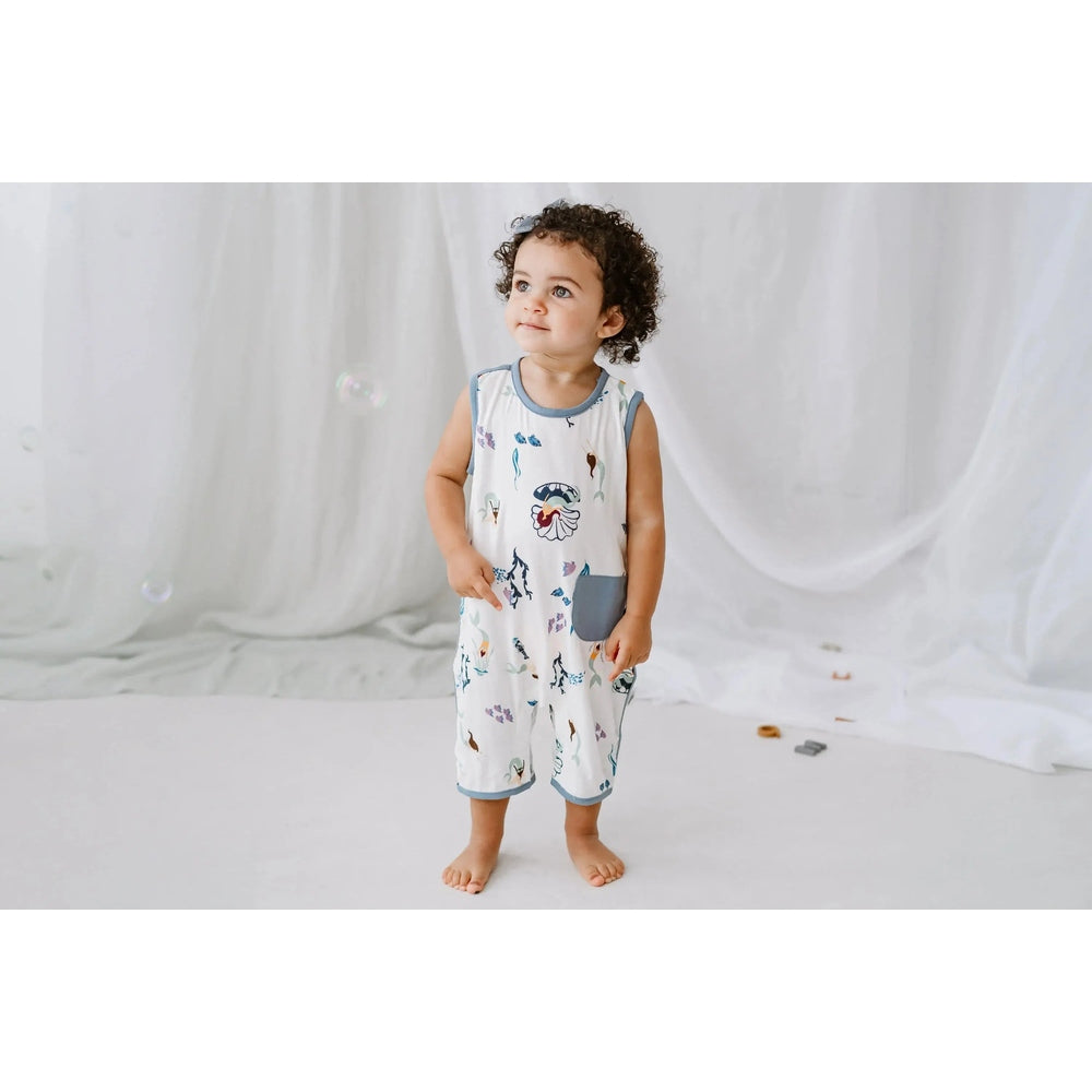 Nest Designs Bamboo Sleeveless Romper Splish Splash, white with blue trim and ocean print pocket, toddler stands barefoot.