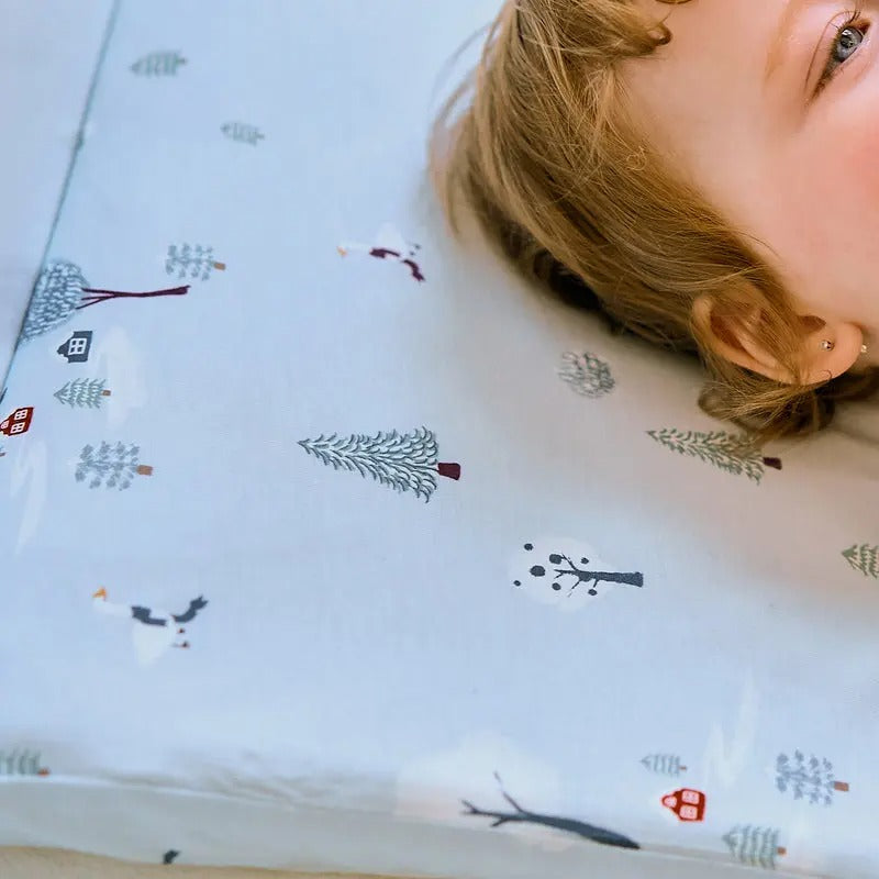 Nest Designs Bamboo Toddler Pillow With Pillowcase Snowy Snuggles, child resting her head on a light-blue tree-pattern pillowcase.