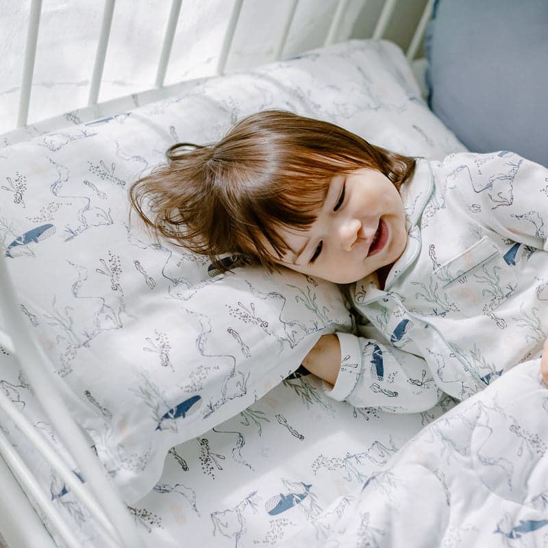 Nest Designs Bamboo Toddler Pillowcase Whale; white pillowcase with blue whale print, child smiling on pillow.