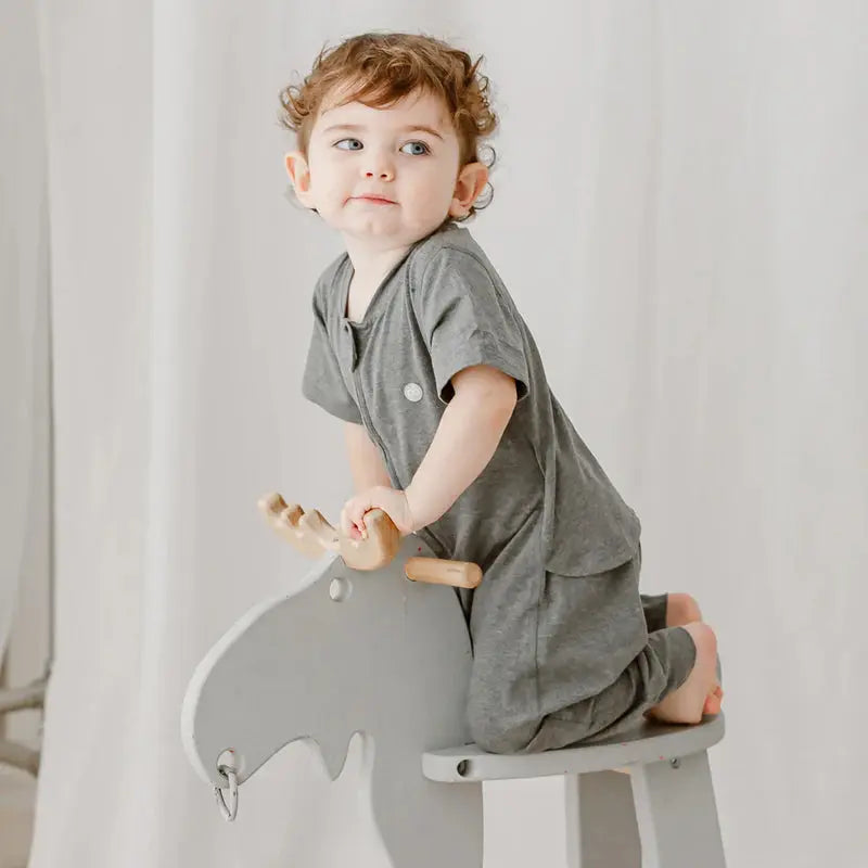 Nest Designs Basics Bamboo Cotton Short Sleeve Drop Bottom Romper Charcoal: toddler sits on a gray rocking horse, gripping wooden handles.