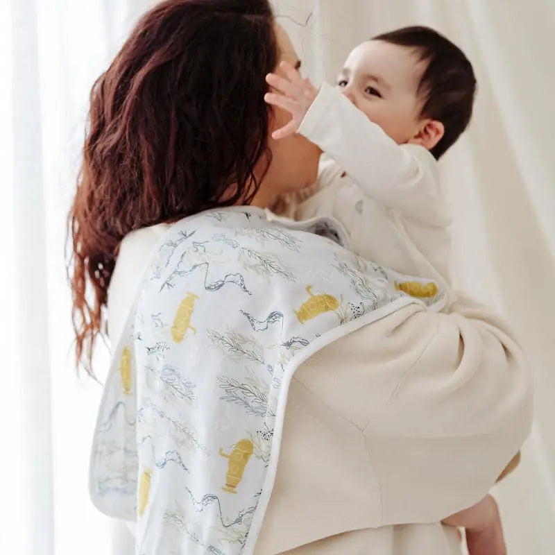 Nest Designs Burp'N Bib 2-pack; white fabric with yellow print, shown draped over mom's shoulder as a burp bib during feeding.