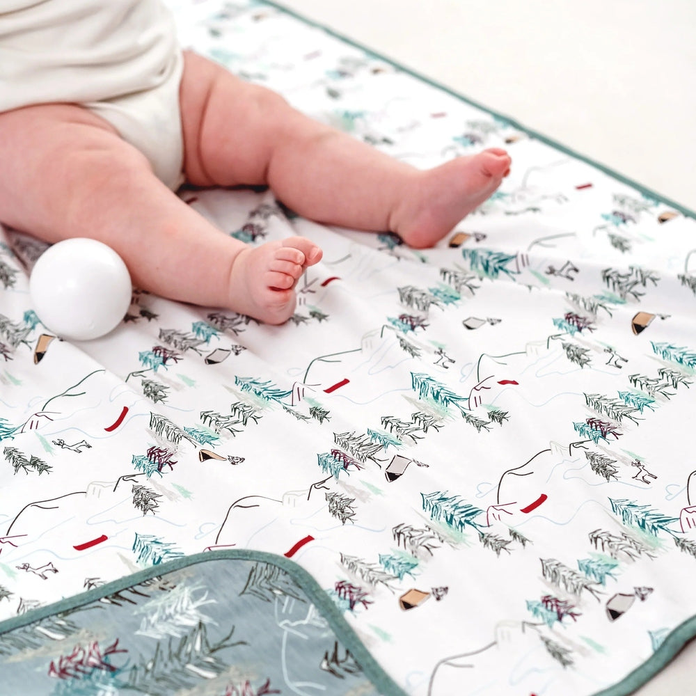 Nest Designs Cotton Waterproof Baby Change Pad Forest Fun; a baby rests on the patterned mat, illustrating its waterproof surface.