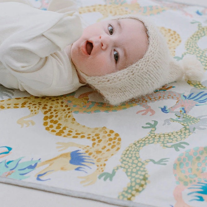 Nest Designs Dragon Dance changing pad, cotton waterproof, on a colorful dragon-pattern mat with a baby