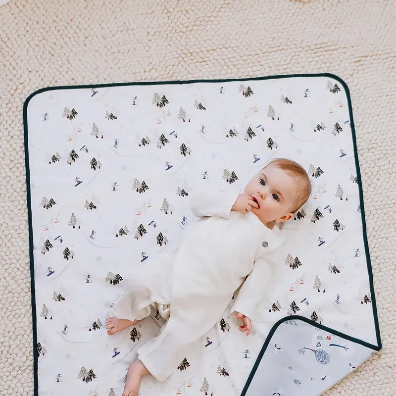 Nest Designs Cotton Waterproof Change Pad Large Winter Fun, white with forest pattern, baby lying on it to show size and softness.
