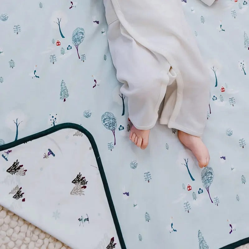 Nest Designs Cotton Waterproof Change Pad Large Winter Fun, baby feet rest on the snowy-patterned surface.