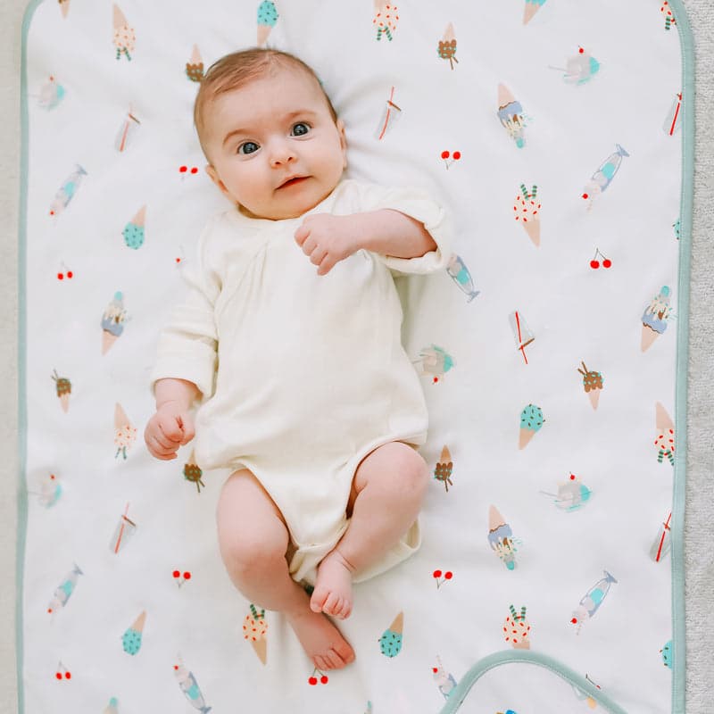 Nest Designs Sweet Treats cotton waterproof change pad with baby lying on a white printed mat