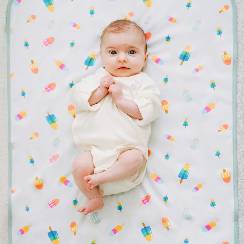 Nest Designs cotton waterproof changing pad Sweet Treats with baby lying on white pad covered in colorful popsicle print
