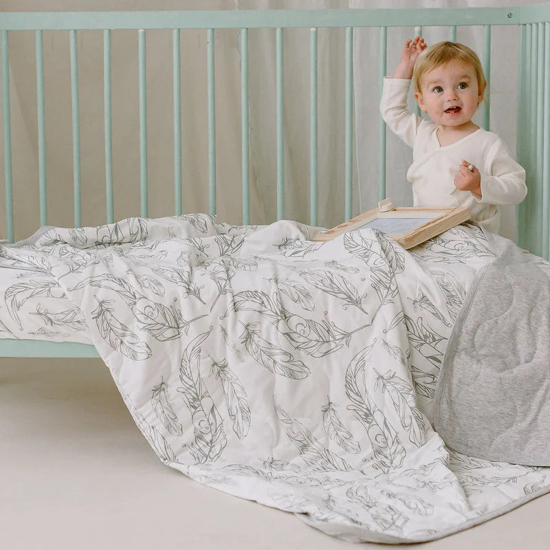 Nest Designs Cozy Blanket Small Feather Grey draped over a crib, showing warmth with a toddler nearby.