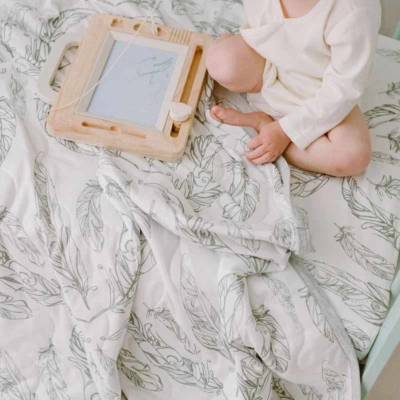 Nest Designs Cozy Blanket Small Feather Grey covering a baby as they play with a wooden frame toy.