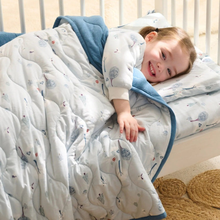 Nest Designs Cozy Blanket Small Snowy Snuggles wraps a smiling child in a blue-edged quilt.