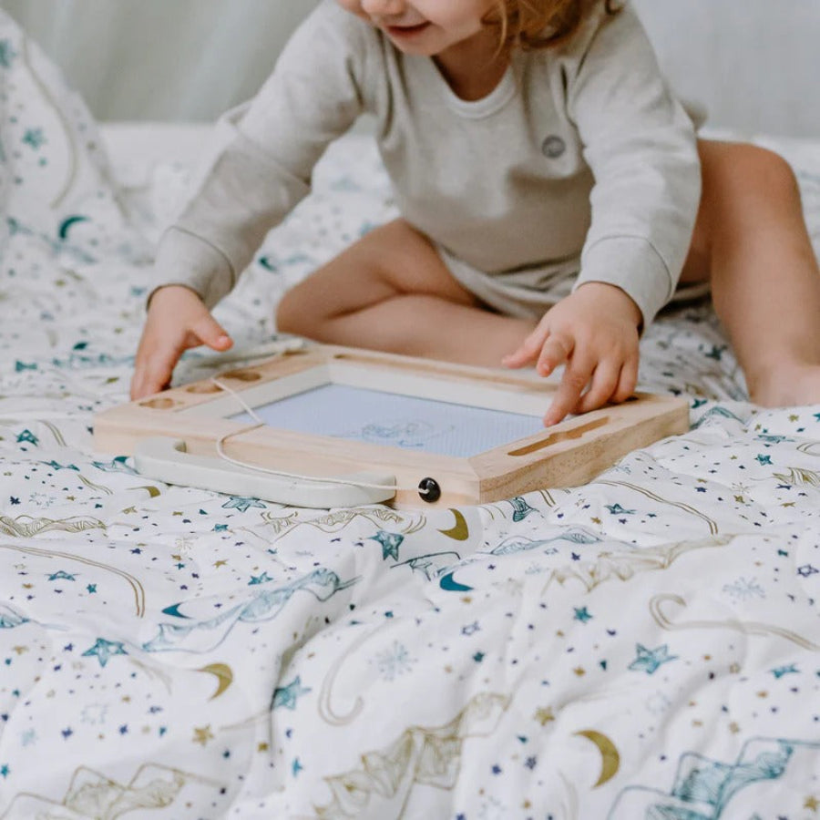 Child on a bed touches the Nest Designs Cozy Blanket Small Stars White, showcasing a soft starry white blanket.