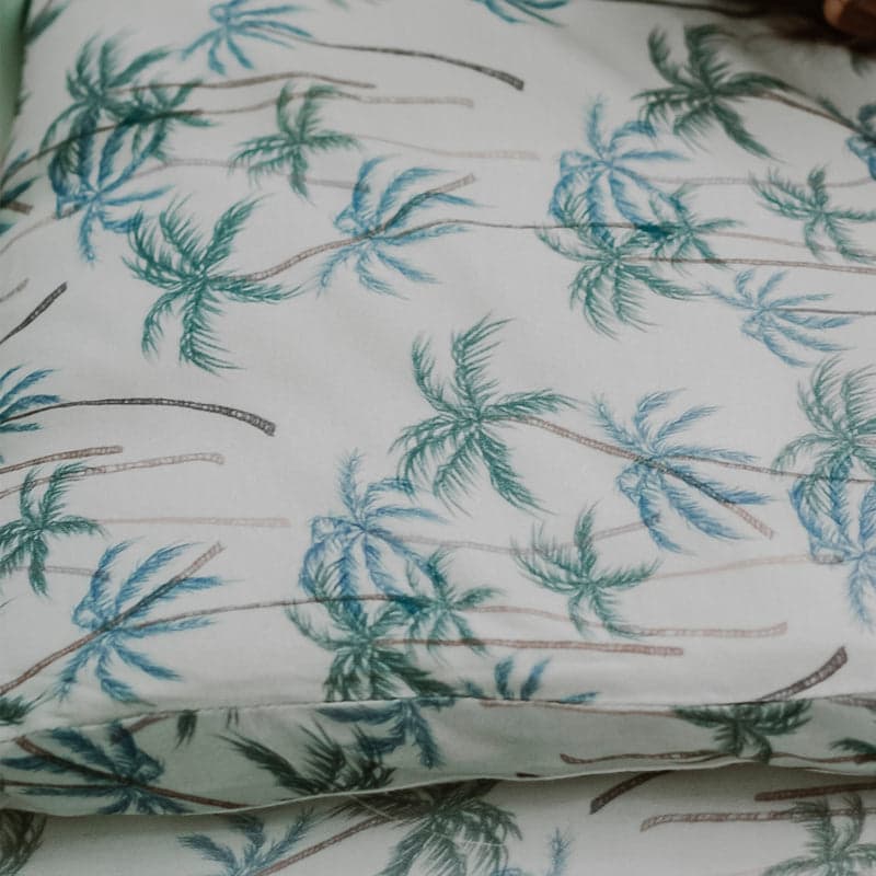 Nest Designs foam pillow with bamboo jersey pillowcase Coco Beach resting on a bed with teal palm-tree print.