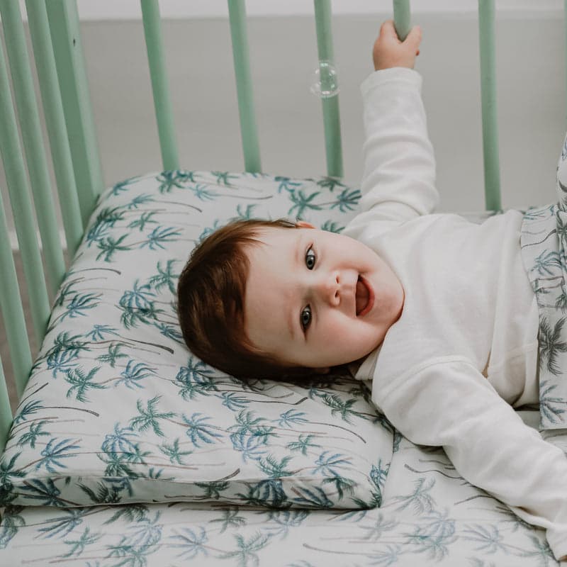 Nest Designs foam pillow with bamboo jersey Coco Beach pillowcase; baby smiles while resting on the crib pillow.