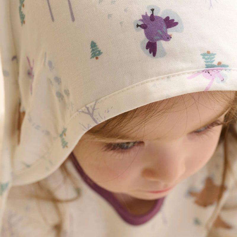 Nest Designs Organic Cotton 9-Layer Hooded Baby Bath Towel Snow Angels; baby wears the hooded towel with snow-angel print.