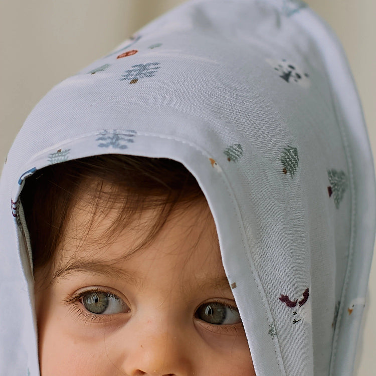 Nest Designs Organic Cotton 9-Layer Hooded Baby Bath Towel Snowy Snuggles; baby wearing the soft white hooded towel with tiny snowflake prints.