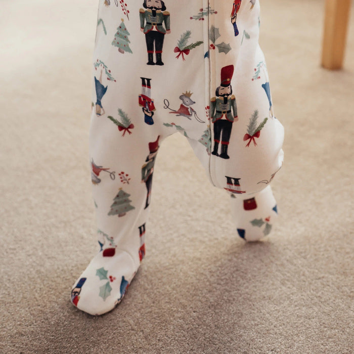 Nest Designs Organic Cotton Long Sleeve Footed Sleeper Nutcracker; cream baby footed onesie with nutcracker print, zipper, baby stepping.