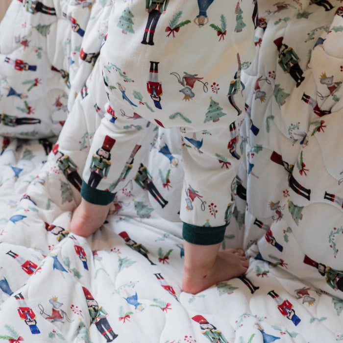 Nest Designs Organic Cotton Long Sleeve Footless Sleeper Nutcracker worn by a baby; white fabric with nutcracker prints and green cuffs