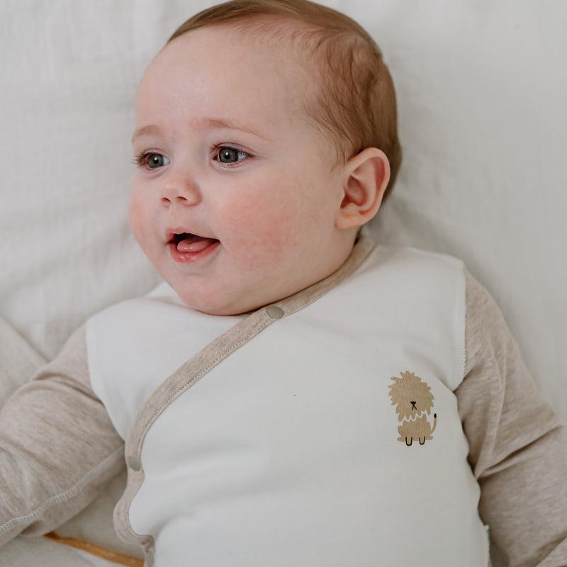 Nest Designs Organic Cotton Long Sleeve Kimono Onesie-Safawhee; baby lies on a white sheet wearing beige sleeves with a small dog graphic.