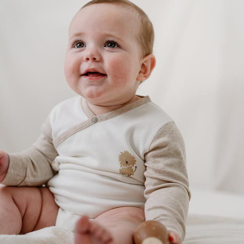 Nest Designs Organic Cotton Long Sleeve Kimono Onesie-Safawhee, cream with beige sleeves, baby smiling while seated.