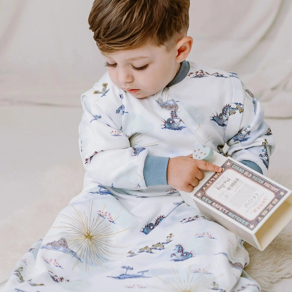 Nest Designs Organic Cotton Removable Long Sleeve Sleep Bag 1.0 Tog Ocean Wonders; baby in ocean-print sleepwear sits and points at a toy.