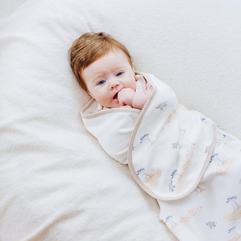 Nest Designs Organic Cotton Startle Stop Sleep Bag 0.5 Tog Baby Baobabs, cream sleep sack gently wrapped around baby on a soft white surface.