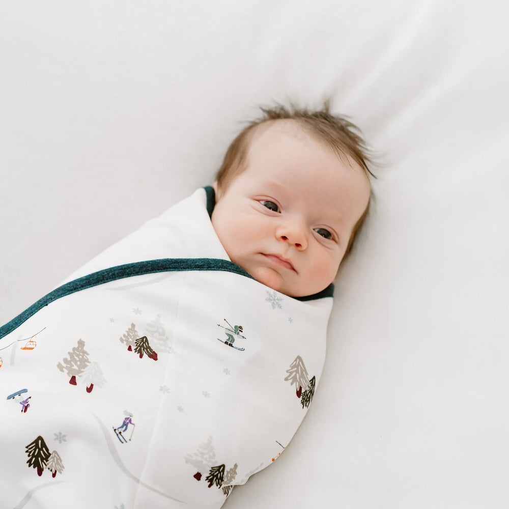 Nest Designs Organic Cotton Startle Stop Sleep Bag 0.5 Tog Chills N' Thrills, white with teal trim, baby wrapped snugly.