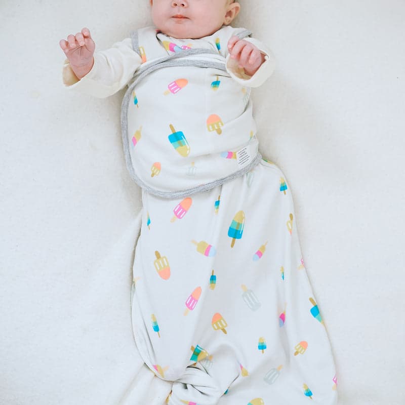 Nest Designs Startle Stop Sleep Bag 0.5 Tog Summer Pops; baby lying on back in white organic cotton sleep sack with colorful popsicles.
