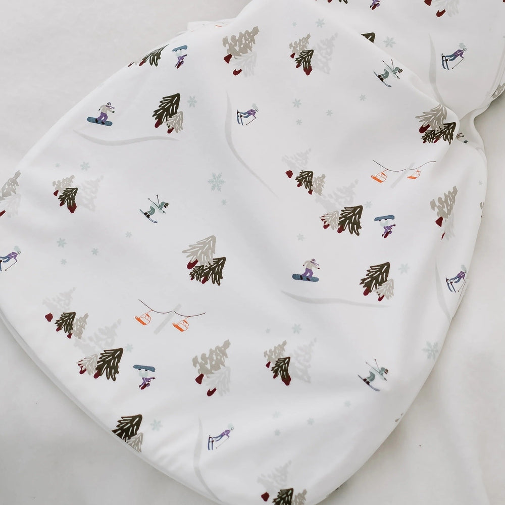 Nest Designs Startle Stop Sleep Bag 0.5 Tog, white with winter trees and skiers, demonstrating soft organic cotton fabric.
