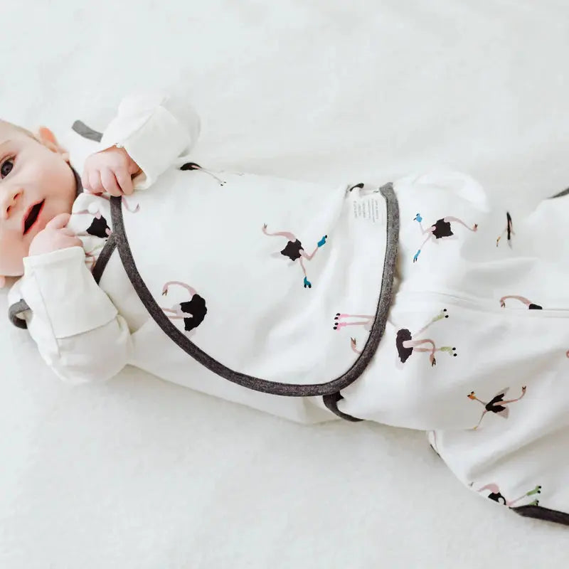 Nest Designs Organic Cotton Swaddle Sleep Bag 1.0 Tog Let's Roll; white ballet-print swaddle keeping baby snug and wrapped.
