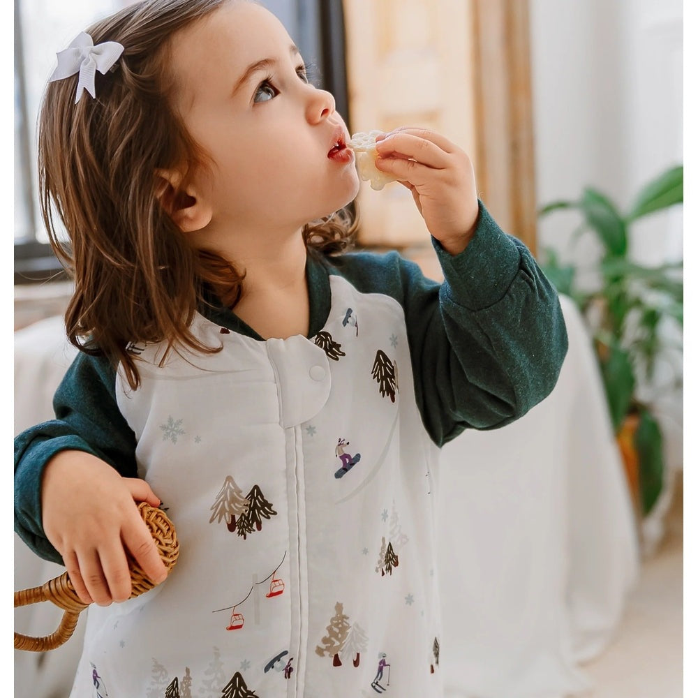 Nest Designs Raglan Bamboo Long Sleeve Footed Sleep Bag 2.5 Tog Chills N' Thrills, baby cozy in a white tree-print sleep bag indoors.