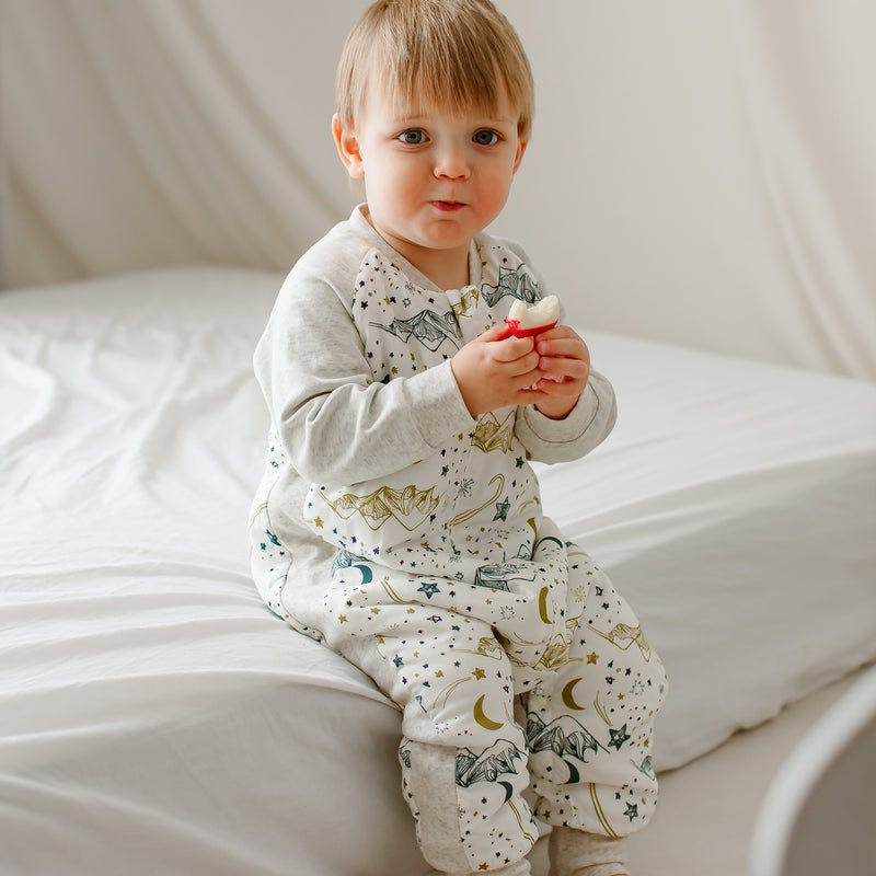 Nest Designs raglan bamboo sleep bag, long-sleeve, footed, 2.5 Tog, stars on white; baby sits on bed with a snack.