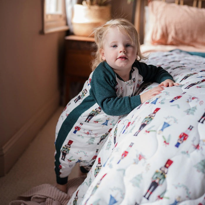 Nest Designs Raglan Bamboo Long Sleeve Footed Sleep Bag 2.5 Tog Nutcracker; toddler in green-sleeved sleep sack stands by bed.