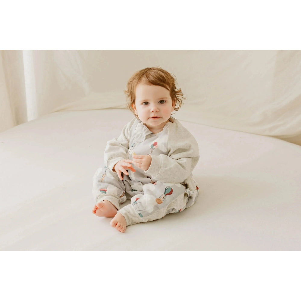 Nest Designs Raglan Bamboo Long Sleeve Footed Sleep Bag 2.5 Tog Meerkats Away; baby sits cozily on a pale bed.