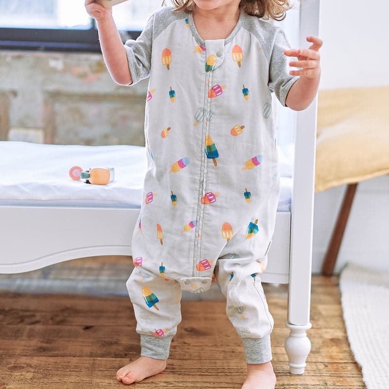 Nest Designs Raglan Bamboo Pima Short Sleeve Footed Sleep Bag 0.6 Tog; light gray with summer popsicle print, toddler standing.